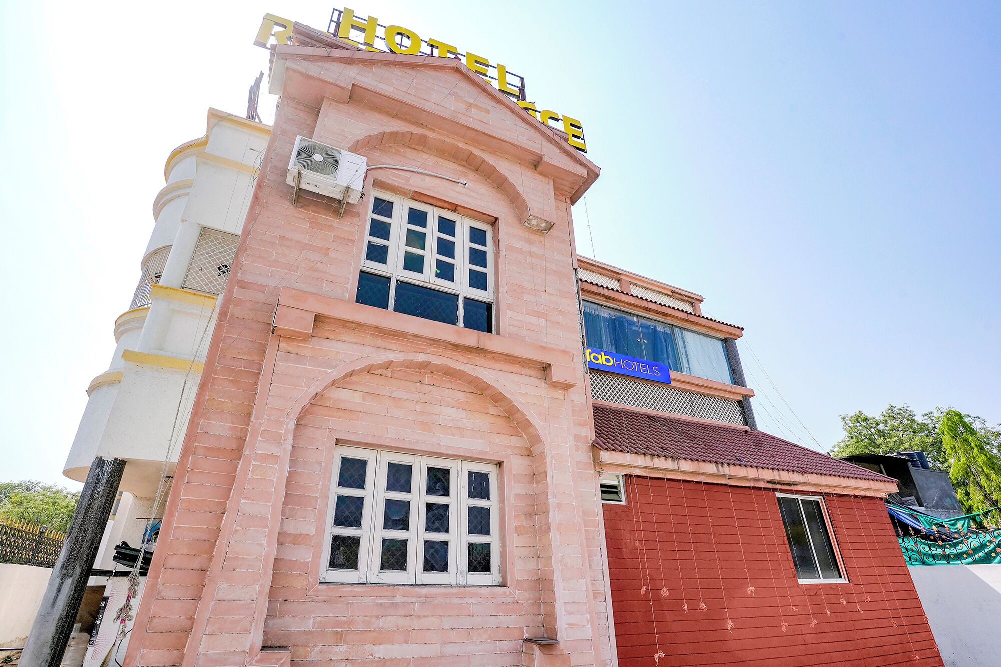 Un hôtel avec une enseigne bien visible, de nombreuses fenêtres et une partie rouge située en bas à droite.