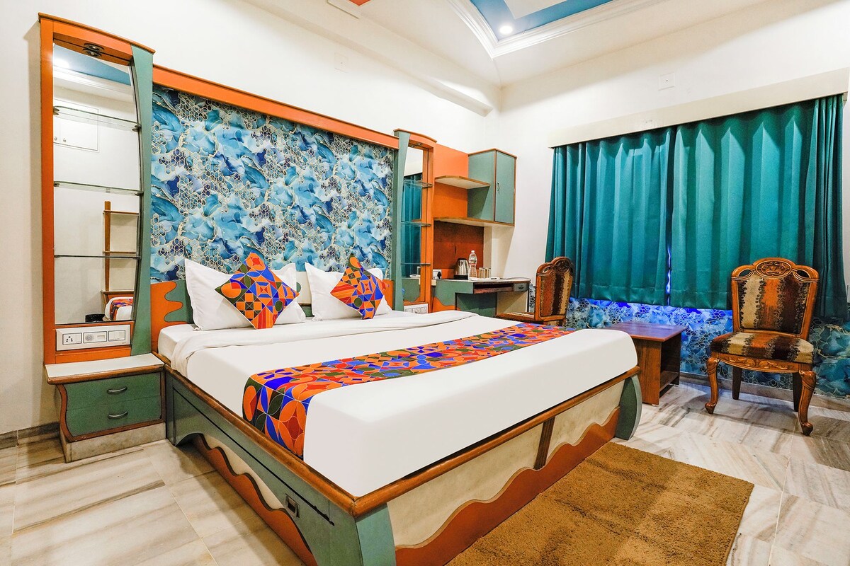 A hotel room with a bed, a desk, a chair, a wardrobe, and a large mirror.