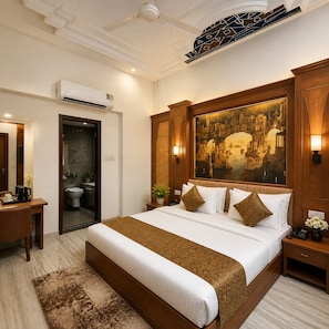 A hotel room with a large bed, a desk, a bathroom, and a painting on the wall. - Hotel Rest & Peace, Airport (Ahmedabad)