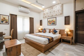 A hotel room with a bed, bedside tables, a desk, an air conditioner, and a window with curtains.