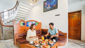 Eine Hotelhalle mit Treppe, einer Rezeption, einem Fernseher und einem Essbereich mit Frühstück.