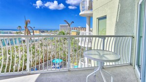 A balcony with a view of the ocean, palm trees, and a building in the background. - ☀️Crystal Palms 405 - Excellent Location and Amenities☀️ (Treasure Island)