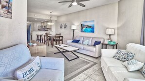 A modern living room with a sofa, coffee table, and a dining area with chairs and a table. - ☀️Crystal Palms 405 - Excellent Location and Amenities☀️ (Treasure Island)