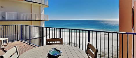 A balcony with a round table and chairs, overlooking a beach.