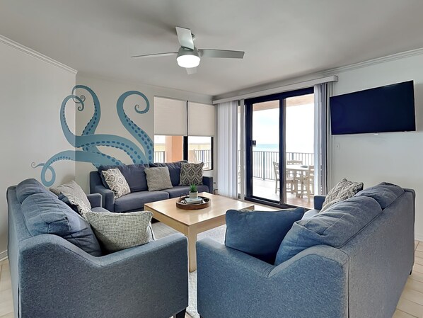 A modern living room with a ceiling fan, a large TV, and a view of the balcony.