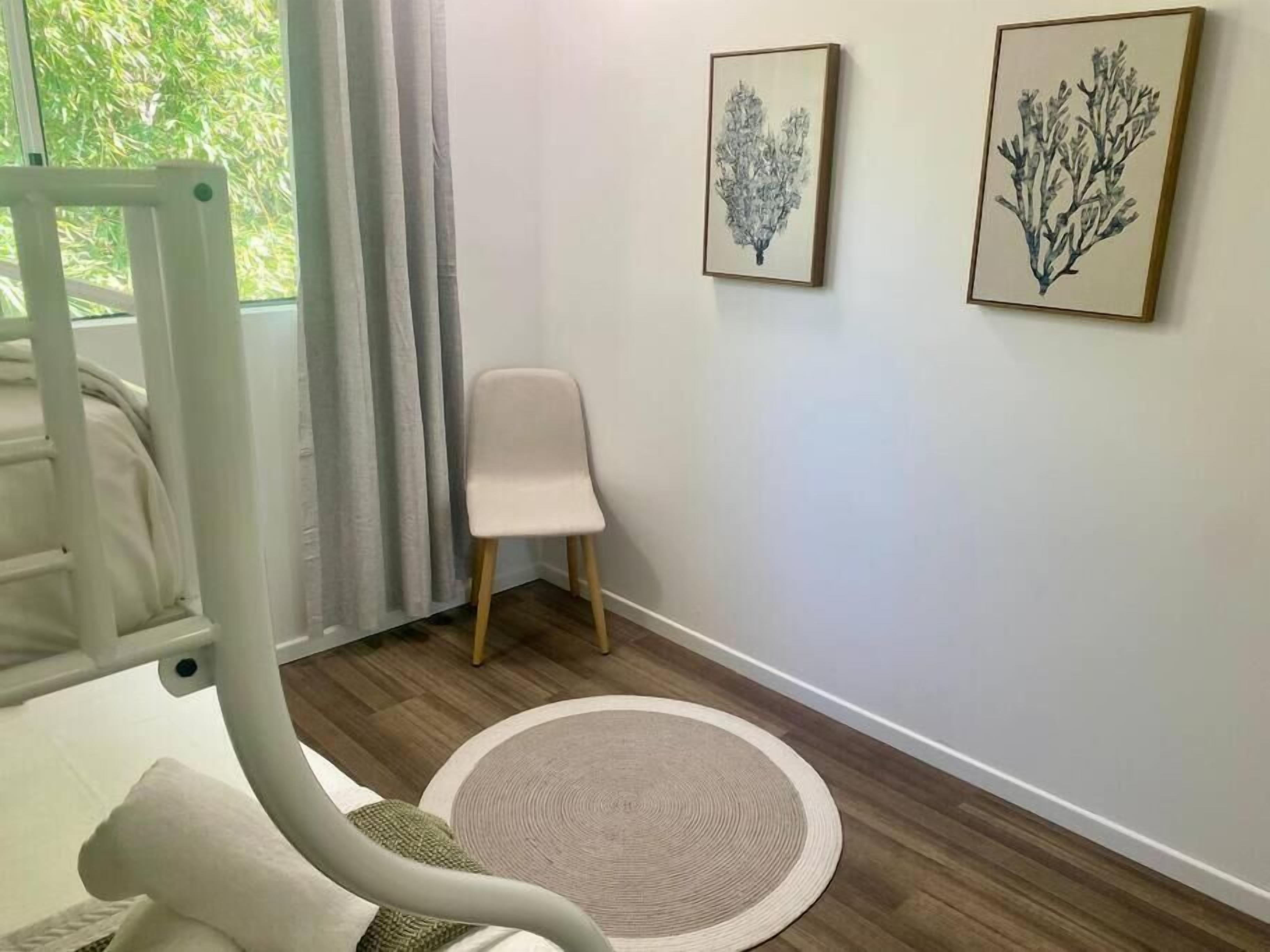 A room with a bed, a chair, a round rug, and two wall-mounted paintings.