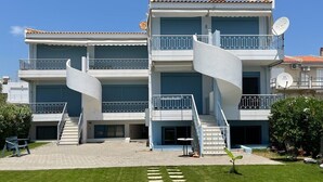 A modern two-story building with a spiral staircase, satellite dishes, and a paved driveway leading to a grassy area with stepping stones.