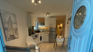 A compact living space with a sofa, a dining table, and a kitchen area including a refrigerator and washing machine.