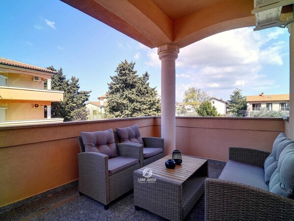 Un balcone con mobili in vimini, un tavolo e una colonna.