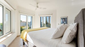 Un dormitorio con una cama, ventilador de techo y ventanas amplias.