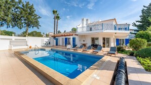 Una casa de dos pisos con piscina, mobiliario exterior y un jardín.