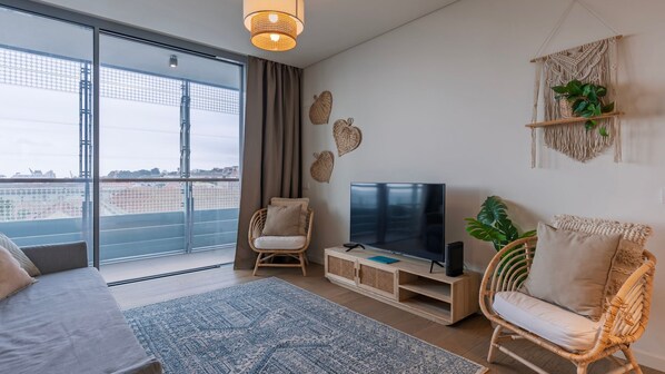 Un salon moderne doté d’un grand téléviseur, de fauteuils en osier, d’un canapé et offrant une vue à travers une porte vitrée.