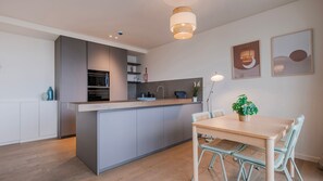 Une cuisine moderne avec des meubles de couleur grise, un îlot central en bois et un coin repas comprenant une table et des chaises.