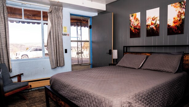 A bedroom with a large bed, a chair, and a window with curtains. - Maverick Motel and Glamp Ground (Raton)