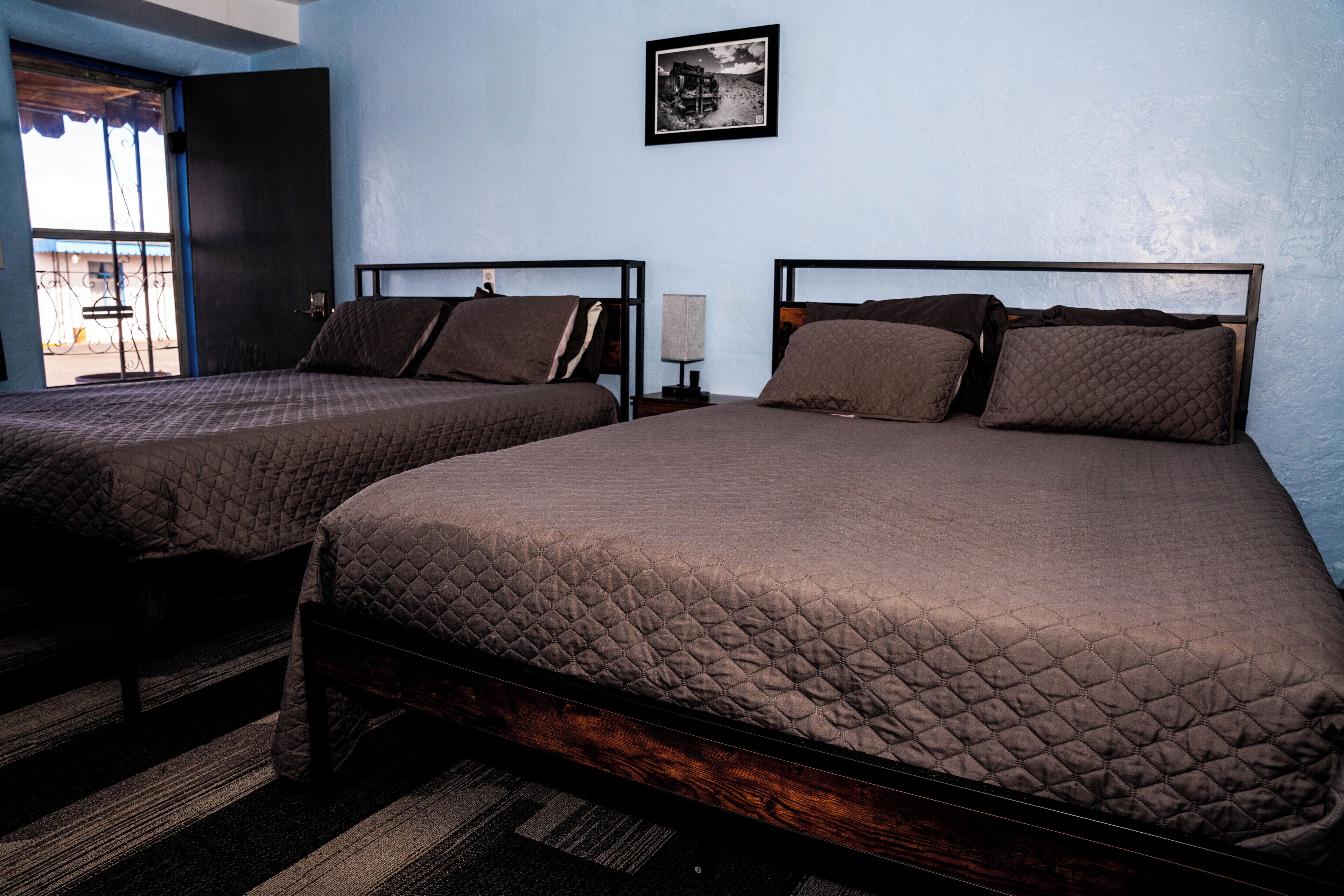 Two single beds with wooden frames and quilted bedding in a room with light blue walls and a black and white picture on the wall.