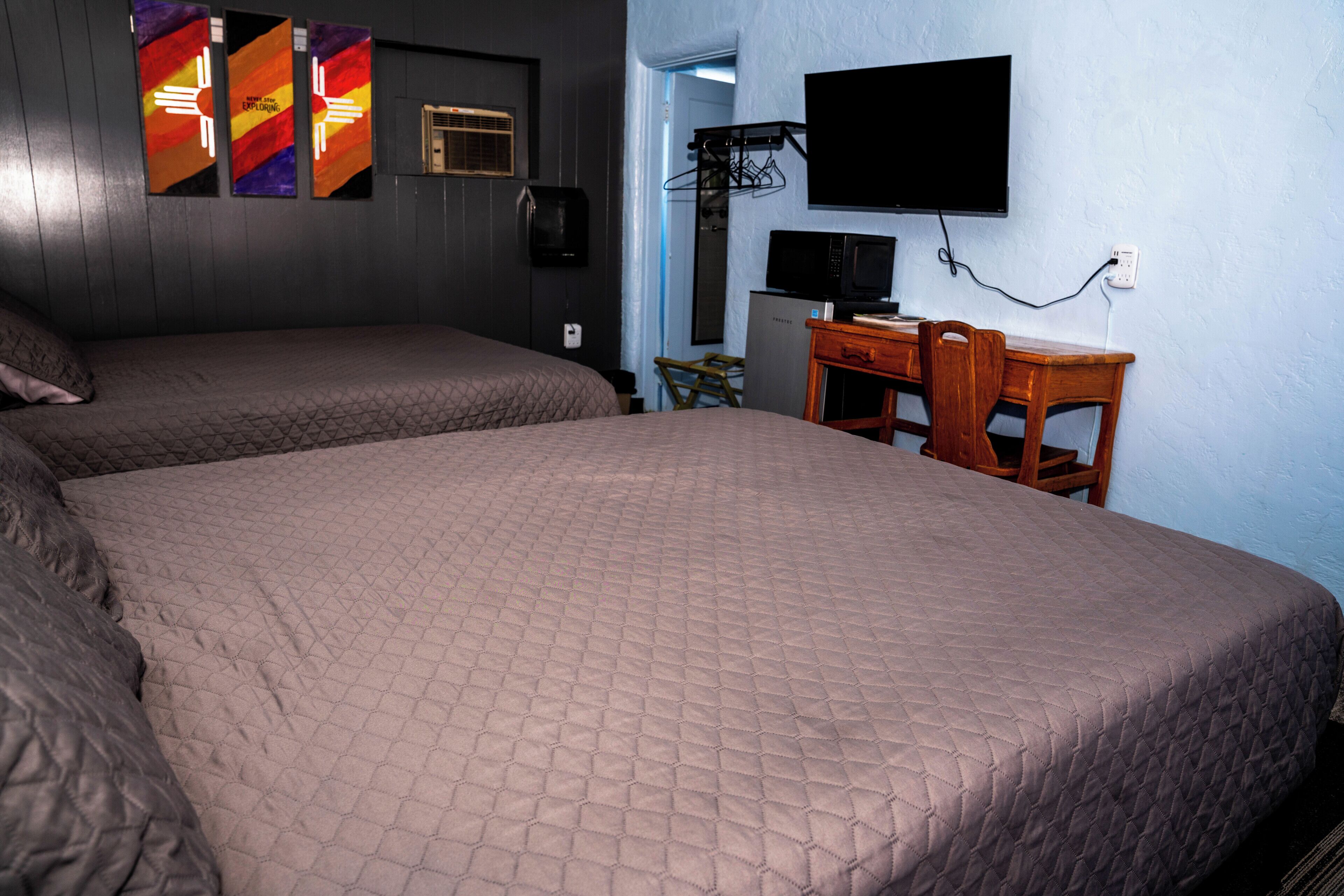 Une chambre d’hôtel avec deux lits, un bureau, une chaise, un téléviseur et un téléviseur fixé au mur.