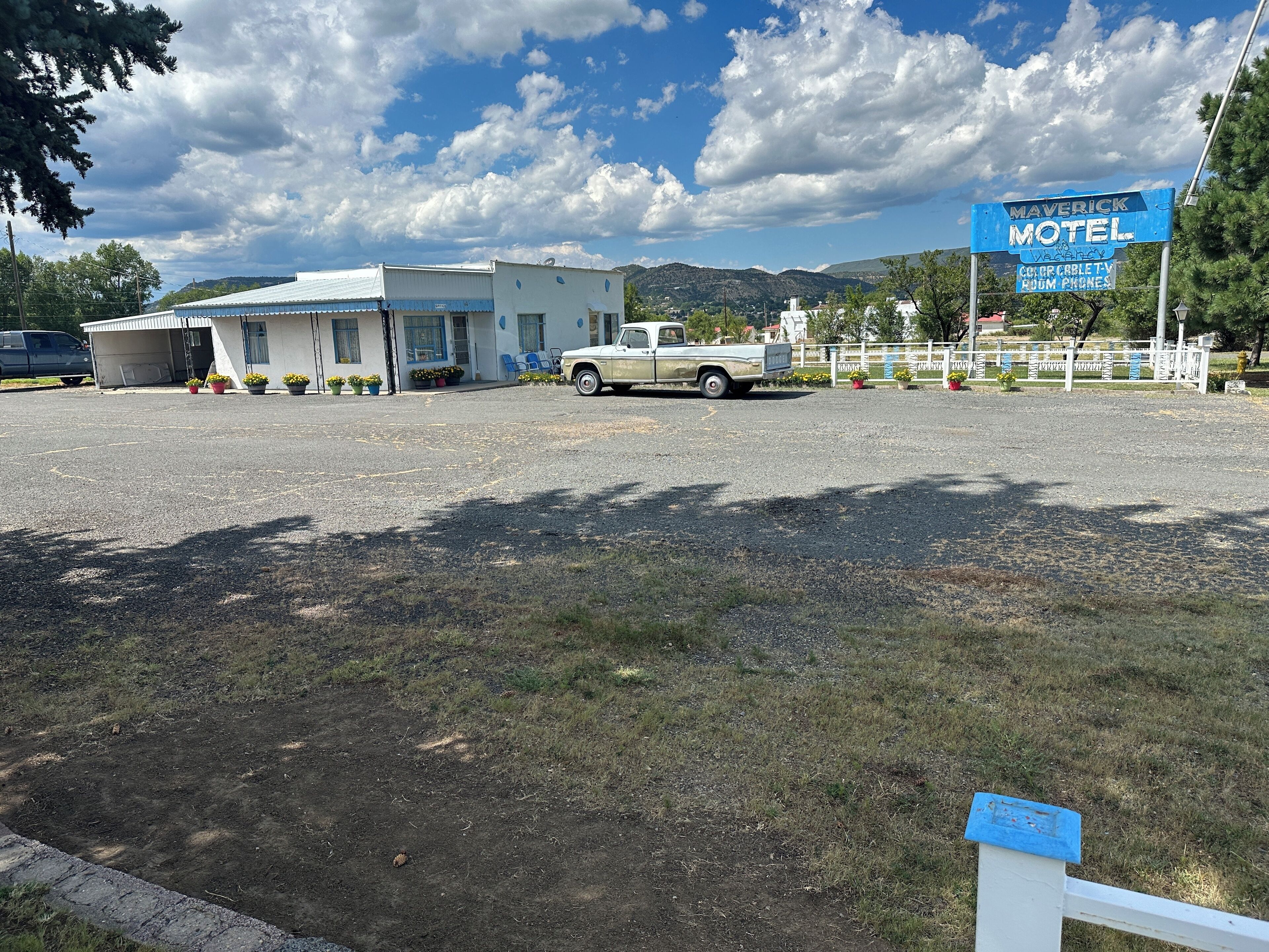 A motel with a white building, a parking lot, and a mountainous background.
