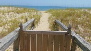 A wooden boardwalk leading to a beach with sand and grass.
