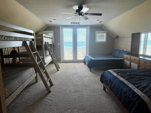 A bedroom with bunk beds, a ceiling fan, a large window, and a dresser.