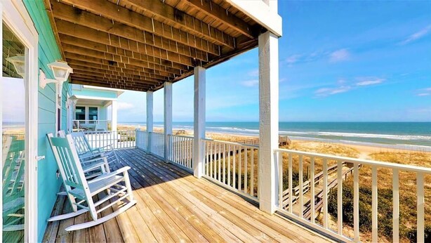 A wooden deck with rocking chairs overlooking a beach.