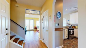 A hallway with a staircase leading to a room, a kitchen with white cabinets, and a tiled floor.