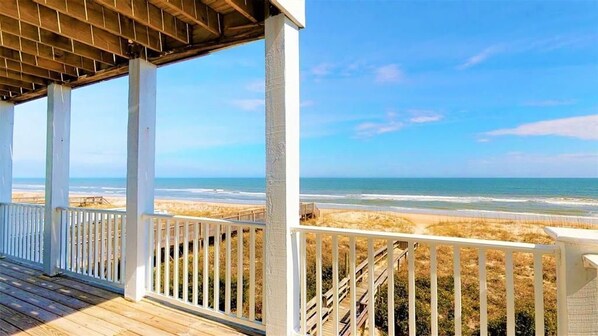 A wooden deck with white railings overlooking a beach.