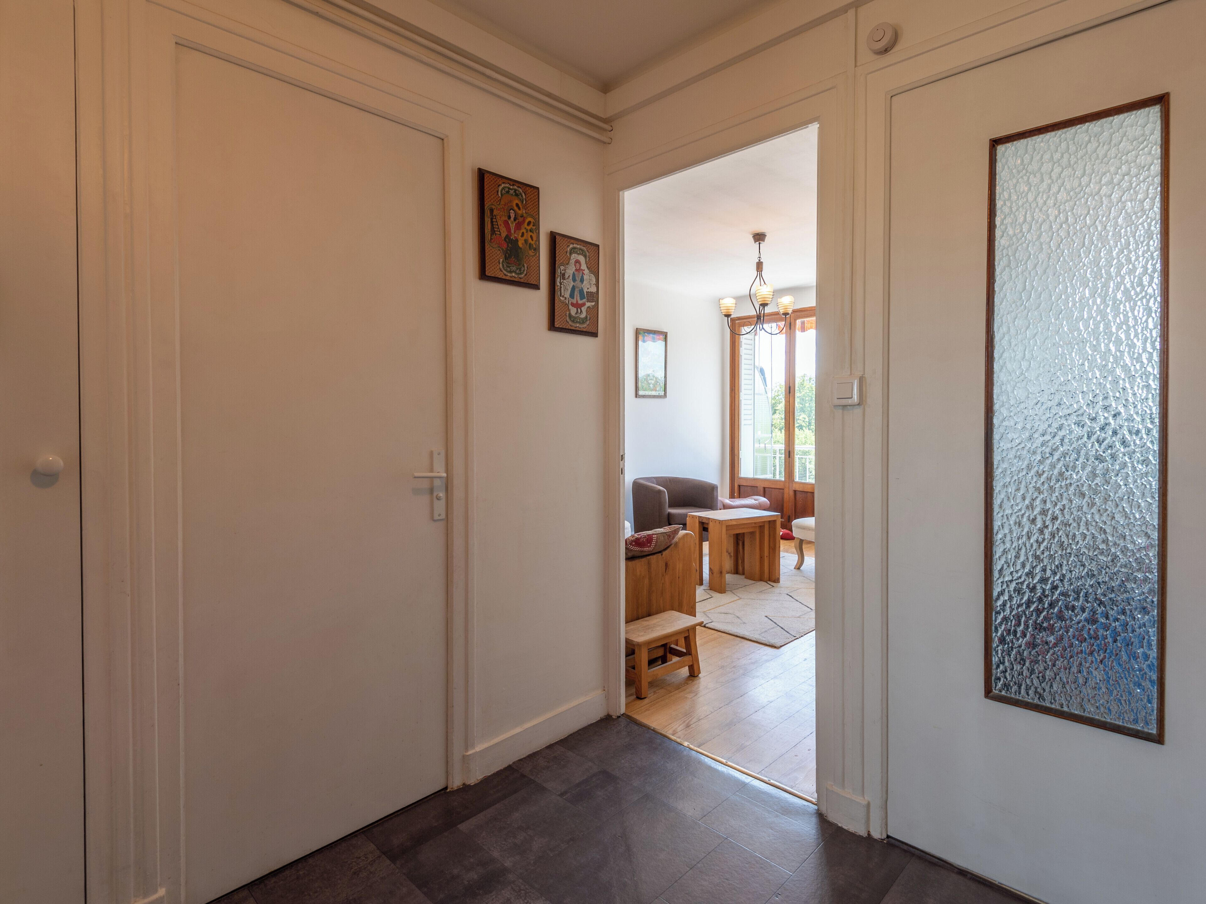 Un couloir doté d’un plancher en bois, d’une porte et d’une vue sur un espace de vie comprenant un canapé et une table.
