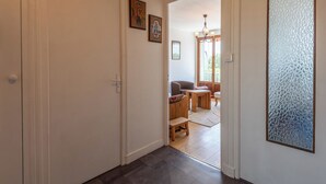 A hallway with a wooden floor, a door, and a view into a living area with a sofa and a table.