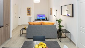 Een moderne hotelkamer met een bed, een televisie, een eettafel met fruit en een klein bijzettafeltje.