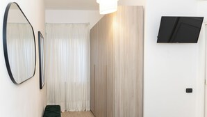 Een gang met een spiegel, een bank, een schuifdeur en een wandtelevisie.