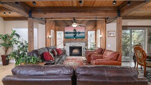 A spacious living room with a fireplace, leather sofas, and a television mounted above it. - RH465- Ultimate Mountain Retreat (Zephyr Cove)