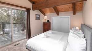A bedroom with a large bed, a wooden ceiling, a sliding glass door to a balcony, a dresser, and a door. - RH465- Ultimate Mountain Retreat (Zephyr Cove)