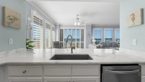 A modern kitchen with a large island, white cabinetry, and a built-in dishwasher.