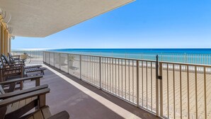 A beachside balcony with wooden chairs and a railing overlooking the ocean.