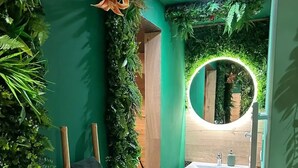 A bathroom with a green wall, a vertical garden, a wooden bench, and a round mirror with a light. - Apartment Cocoon jungle, romantic loveroom (Altkirch)