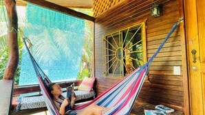 A hammock in a wooden room with a wooden ceiling and a window with a yellow frame. - Casa Yamann (Manzanillo)