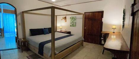 Un dormitorio con cama con dosel, ventilador de techo, mesita de noche con lámpara y puerta que da a otra habitación.