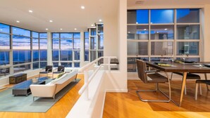 A spacious room with a large window offering a view of the sky, a dining area with a table and chairs, and a seating area with a sofa and chairs. - Stunning Panoramic Ocean Views Penthouse (Manhattan Beach)