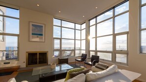 A spacious living room with a large window, a fireplace, a sofa, and a coffee table. - Stunning Panoramic Ocean Views Penthouse (Manhattan Beach)
