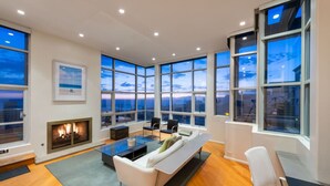 A spacious living room with a fireplace, large windows, and a modern sofa. - Stunning Panoramic Ocean Views Penthouse (Manhattan Beach)