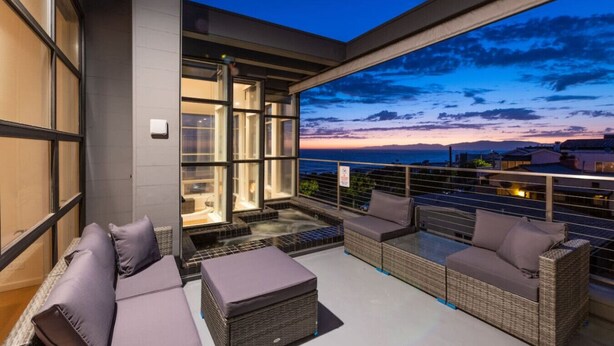 A balcony with a hot tub, seating, and a view of the ocean at dusk. - Stunning Panoramic Ocean Views Penthouse (Manhattan Beach)
