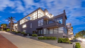A modern multi-story building with large windows and a flat roof, surrounded by greenery and a paved driveway. - Stunning Panoramic Ocean Views Penthouse (Manhattan Beach)