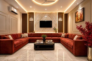 A modern living room with a sectional sofa, a flat-screen TV, and a marble floor. - Hotel Kelvish by Foxi Group (New Delhi)