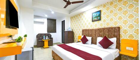 A hotel room with a bed, a desk, a chair, a television, and a ceiling fan.