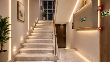 Una escalera de mármol conduce a una puerta, con un letrero de salida de incendios en la pared y una planta en maceta a la izquierda.