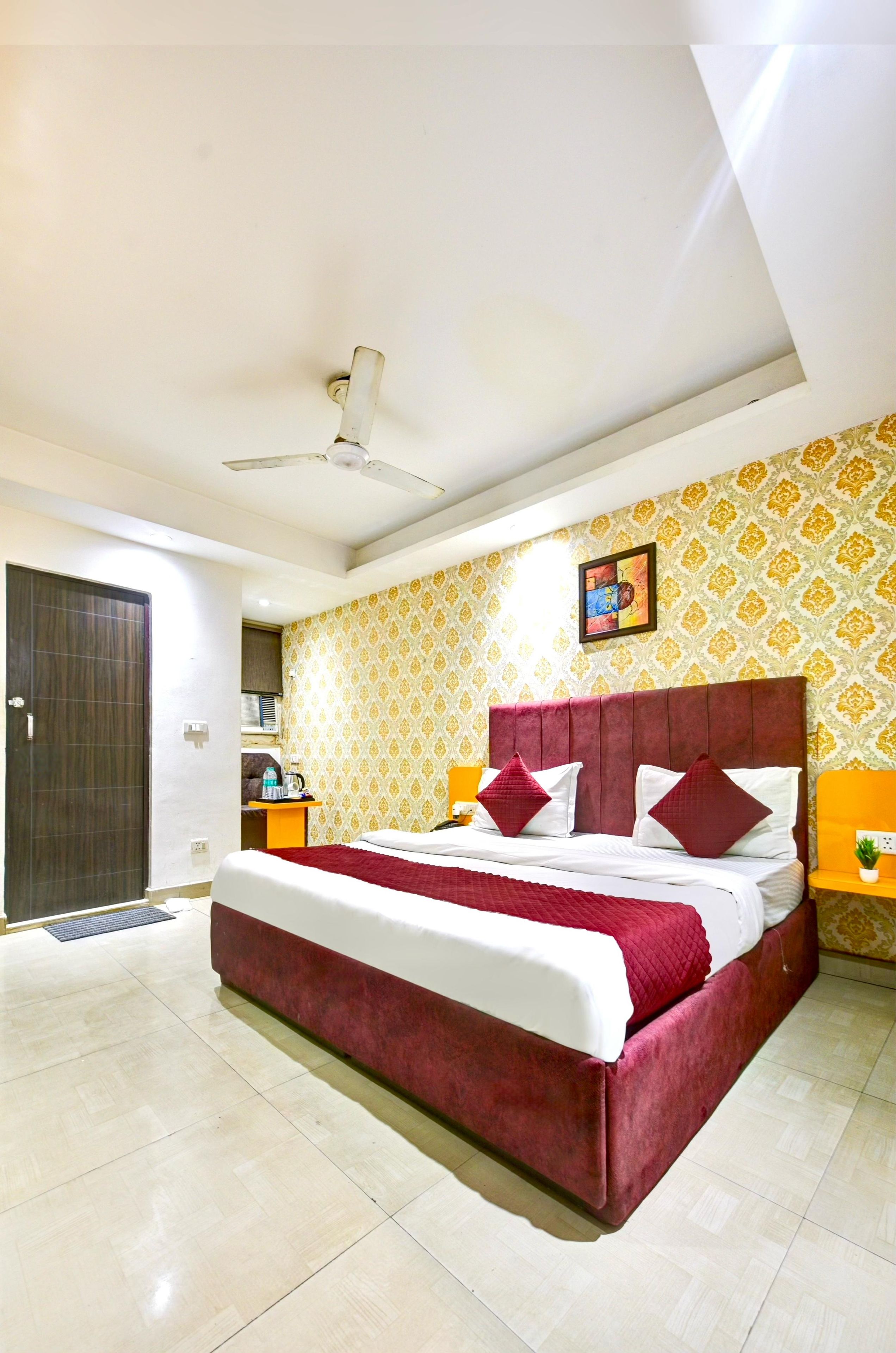 A hotel room with a bed, a ceiling fan, a patterned wallpaper, and a door.