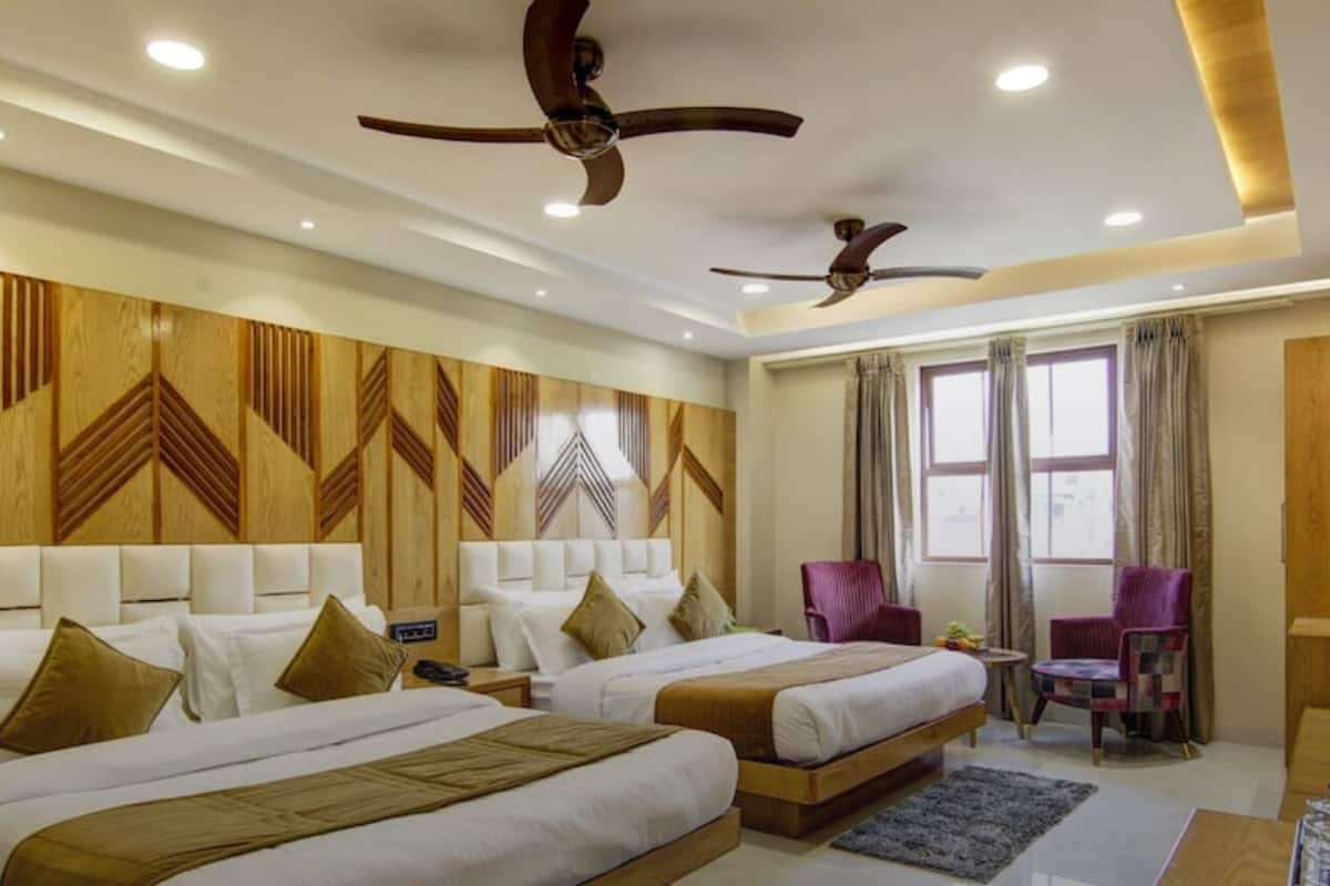 Une chambre d’hôtel avec deux lits, une tête de lit en bois, des ventilateurs de plafond et une fenêtre avec des rideaux.