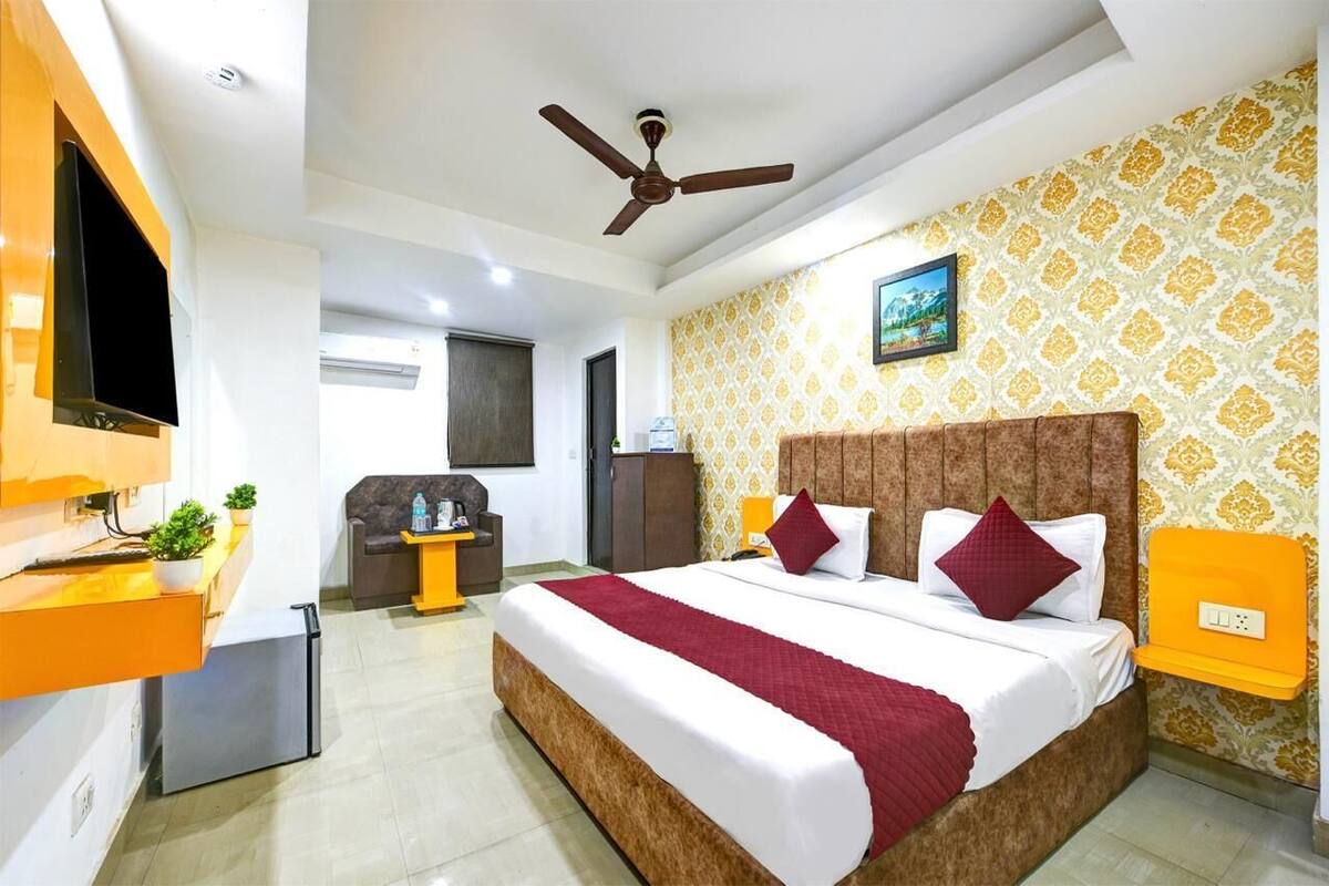 Une chambre d’hôtel équipée d’un lit, d’un ventilateur de plafond, d’une télévision, d’un petit réfrigérateur, d’un bureau et d’une étagère fixée au mur.