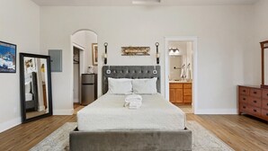 A bedroom with a bed, a dresser, a mirror, and a door leading to a bathroom.