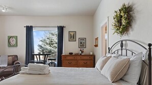 Une chambre d’hôtel avec un lit, une commode en bois, une petite table avec une chaise et une fenêtre avec des rideaux.